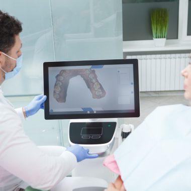 # Cum simplifică 3DentaSoft relația dintre medicul stomatolog și tehnicianul dentar Pe colțul unui birou de recepție stă un plic maro cu numele pacientului scris de mână. Înăuntru, o amprentă de silicon, o fișă completată în grabă și un bilețel cu nuanța aleasă. Plicul așteaptă curierul, curierul așteaptă traficul, iar tehnicianul dentar așteaptă să vadă ce a primit. Cam așa a arătat, ani la rând, colaborarea dintre un cabinet stomatologic și un laborator dentar. Doi profesioniști care lucrează la același pacient, uneori la câteva sute de kilometri distanță, care nu se văd niciodată la față și care comunică prin obiecte fizice și prin telefoane date între două consultații. Cele mai multe frustrări din protetică nu vin din lipsă de competență, ci din traducerea greșită a intenției dintr-un cap în altul. ## Ce se pierde de fapt între cabinet și laborator Un medic bun știe exact ce vrea. Problema apare când trebuie să pună asta pe hârtie, într-o rubrică de trei rânduri, la sfârșitul unei zile în care a avut unsprezece pacienți. Scrie "coroană zirconiu 26, A3", pune amprenta în plic și pleacă acasă convins că a spus tot. Tehnicianul deschide plicul a doua zi. Vede o amprentă cu o bulă de aer fix în zona pragului, o antagonistă turnată aproximativ și o nuanță care nu spune nimic despre translucența dinților vecini. Poate sună, poate nu. Iar dacă sună, prinde medicul în plină anestezie, discuția se amână pentru seară, seara se uită amândoi, și uite așa dispar două zile din termenul promis pacientului. Aici se naște cea mai mare parte a tensiunii. Nu din rea-voință, ci dintr-un lanț de informații incomplete care circulă încet și prin prea multe mâini. Fiecare verigă adaugă o mică pierdere, iar la capăt iese o lucrare care are nevoie de ajustări în cabinet. ### Distanța ca problemă de business, dincolo de logistică Un cabinet din Botoșani care găsește un tehnician foarte bun în București lucrează, practic, cu un handicap de două zile la fiecare comandă. Cei mai mulți medici renunță și rămân la laboratorul din colț, chiar dacă rezultatele nu îi mulțumesc. S-a format astfel o piață ciudată, în care calitatea unei lucrări depinde mai mult de codul poștal al cabinetului decât de competența disponibilă în țară. Un tehnician excelent din Cluj nu putea servi un medic din Constanța, oricât și-ar fi dorit amândoi. Fluxul digital a rupt legătura asta dintre geografie și acces. ## Momentul în care fișierul a înlocuit gipsul Scanerul intraoral nu e o noutate absolută, apare prin cabinetele europene de mai bine de un deceniu, dar abia în ultimii ani a devenit accesibil unui cabinet mediu din România. Ce schimbă el trece dincolo de confortul pacientului, deși și ăsta contează enorm pentru oricine a ținut vreodată o lingură cu silicon în gură. Se schimbă natura obiectului care circulă între medic și tehnician. Un fișier STL nu se deformează la transport, nu se rupe, nu se pierde la curier și, mai important decât toate, poate fi verificat pe loc. Medicul vede pe ecran, înainte să lase pacientul din scaun, dacă pragul e complet, dacă a prins suficient din dinții vecini, dacă ocluzia s-a înregistrat corect. Când ceva nu arată bine, rescanează zona în două minute. Pacientul e încă acolo, anestezia e încă activă, nimeni nu trebuie chemat înapoi peste trei zile. Prima verificare de calitate se mută din laborator în cabinet, adică exact acolo unde corectarea costă cel mai puțin. ## Comanda care nu se mai pierde pe drum Partea a doua a poveștii, cea despre care se vorbește mai rar, e ce se întâmplă cu fișierul după ce a fost salvat. Aici intră platformele de comandă online, iar **[primul laborator dentar 100% online din România](https://www.3dentasoft.com)** s-a construit exact în jurul acestei idei, transformând comanda dintr-un plic într-o pagină pe care medicul o completează în cinci minute. Diferența pare mică pe hârtie. În practică, o comandă digitală impune un minim de disciplină pe care fișa scrisă de mână nu l-a cerut niciodată. Nu poți trimite comanda fără tipul lucrării, materialul, dinții implicați și nuanța, fiindcă formularul nu te lasă mai departe. Tehnicianul primește un pachet complet. Are fișierul de scanare, fotografiile intraorale, nuanța documentată cu cheia de culori lângă dinte și notele medicului scrise când avea cazul proaspăt în minte. Nu mai ghicește nimic și nu mai trebuie să sune. ### Istoricul care rezolvă discuțiile de mai târziu Un beneficiu discret al comenzii online e că lasă urmă. Peste patru luni, când pacientul revine cu o nemulțumire, oricare dintre cei doi deschide comanda și vede ce s-a cerut, ce s-a trimis, când s-a livrat și ce ajustări s-au făcut pe parcurs. Am văzut destule colaborări bune care s-au stricat dintr-o discuție de genul "eu ți-am spus altceva". Când totul e documentat, discuția asta nu mai are de unde să înceapă. Rămâne problema tehnică reală, care de obicei se rezolvă în cinci minute de conversație civilizată. ## Designul CAD ca limbaj comun între cei doi profesioniști Aici se petrece poate cea mai interesantă schimbare de dinamică. În fluxul clasic, medicul afla cum arată lucrarea abia când o vedea pe masă, gata făcută. Dacă nu îi plăcea forma, era prea târziu și se refăcea. În fluxul digital, tehnicianul trimite designul înainte să pornească freza. Medicul deschide fișierul, se uită la conturul cervical, la punctele de contact, la relația cu antagoniștii, apoi spune "mai deschide ambrazura distală" sau "coboară cu jumătate de milimetru cuspidul mezio-vestibular". Modificarea durează câteva minute în software, nu o zi de muncă manuală. Ce se întâmplă în timp e că cei doi ajung să vorbească aceeași limbă. Medicul învață constrângerile de design, tehnicianul învață preferințele clinice ale medicului respectiv, iar după vreo zece cazuri împreună aprobările devin formalitate. Relația se maturizează mult mai repede decât în fluxul pe plicuri, unde fiecare învață din greșeli scumpe. ## Producția care nu mai depinde de mâna care a făcut designul Un laborator dentar digital desparte două lucruri care înainte erau lipite unul de altul. Cine gândește lucrarea și cine o produce fizic. Designul se face pe calculator, iar execuția intră pe echipamente care respectă fișierul cu o toleranță pe care mâna omenească nu o atinge constant. Frezarea acoperă zirconia, PMMA, discurile de ceară și compozitele frezabile. Topirea selectivă cu laser, cunoscută sub numele de SLM, scoate schelete metalice cu o densitate și o precizie de adaptare pe care turnarea clasică le obținea rar. Printarea 3D se ocupă de modele, gutiere, machete și lucrări provizorii, adesea peste noapte. Pentru medic, efectul se traduce într-o variabilitate mult mai mică. Coroana livrată luni și coroana livrată peste trei săptămâni ies din același proces, cu aceiași parametri. Predictibilitatea e, până la urmă, ceea ce cumpără un cabinet de la un laborator, mai mult decât frumusețea unei singure lucrări reușite. ### De ce contează centrul de frezare și pentru tehnicianul independent Un tehnician care lucrează pe cont propriu nu își permite o freză de cinci axe, o instalație SLM și un printer profesional. Investiția depășește ce poate amortiza dintr-un volum obișnuit de comenzi. Modelul online rezolvă asta elegant. Tehnicianul face designul, trimite fișierul spre producție, primește piesa frezată sau sinterizată și se ocupă de partea în care chiar excelează, adică stratificarea, caracterizarea și finisarea estetică. Nu mai concurează cu laboratoarele mari pe capital, ci pe pricepere, ceea ce e mult mai sănătos pentru toată lumea. ## Termenele care devin previzibile, în sfârșit Orice medic care a promis unui pacient o lucrare pentru vineri și a primit-o marți știe cât de scump costă asta. Nu în bani, în credibilitate. Pacientul nu înțelege lanțul de producție, el înțelege doar că i s-a spus vineri. Într-un flux digital, termenul se calculează pe etape măsurabile, de la recepția fișierului până la expedierea lucrării finite, cu design, aprobare, producție și finisare între ele. Fiecare etapă are o durată cunoscută, iar o întârziere se vede în momentul în care apare, nu la sfârșit. Marea diferență nu stă neapărat în viteză, deși și ea crește. Stă în faptul că medicul află din timp când ceva merge prost, așa că poate reprograma pacientul cu o săptămână înainte, nu cu o oră. Asta salvează mult mai multe relații cu pacienții decât o zi câștigată la producție. ## Refacerile și conversația despre cine a greșit Nicio lucrare nu iese perfect de fiecare dată, indiferent de tehnologie. Diferența stă în cât de repede afli unde s-a rupt lanțul și cât de calmă e discuția care urmează. Cu amprentă fizică, discuția e aproape imposibil de închis. Medicul zice că amprenta era bună, tehnicianul zice că avea o retracție insuficientă la mezial, iar amprenta a fost aruncată de trei zile. Rămân două opinii și o lucrare de refăcut, plătită de cineva care se simte nedreptățit. Cu fișier digital, amândoi se uită la același obiect. Se vede dacă pragul a fost înregistrat complet, se vede unde a rămas sânge sau salivă, se vede dacă antagonista a fost scanată în ocluzie corectă. Nu mai e o discuție despre vinovăție, e una despre date, iar oamenii se ceartă mult mai puțin când privesc aceeași imagine. ## Ce câștigă concret tehnicianul dentar din aranjamentul ăsta Se vorbește mult despre avantajele medicului și mult prea puțin despre cealaltă parte a mesei. Nedrept, fiindcă tehnicianul e cel care duce greul detaliului. Cel mai vizibil câștig e dispariția muncii fizice fără valoare adăugată. Turnarea modelelor, decuparea bonturilor și montarea în articulator înseamnă ore de manoperă care nu îmbunătățesc cu nimic rezultatul final, doar îl fac posibil. Într-un flux digital, modelul se printează atunci când e nevoie de el, altfel nici nu există. Vine apoi accesul la clienți din toată țara. Un tehnician cu mână bună din Timișoara poate lucra pentru cabinete din Iași, Suceava sau Craiova fără să depindă de curieri și de amprente care se deformează pe drum. Piața lui nu mai e orașul, ci țara. Și mai e ceva, despre care aud rar pe cineva vorbind. Timpul recuperat se întoarce în partea artistică a meseriei, în stratificarea unei fațete, în caracterizarea unui incisiv, în potrivirea unei nuanțe dificile la un pacient tânăr. Astea sunt lucrurile pentru care omul a ales meseria, nu turnatul gipsului la ora nouă seara. ## Costurile care dispar fără să le fi numărat cineva vreodată Cabinetele calculează prețul lucrării și atât. Restul cheltuielilor rămân invizibile fiindcă nu apar pe nicio factură. Se adună din siliconul și lingurile consumate, din gips, din curierat, din telefoanele date, din timpul asistentei care ambalează și urmărește coletele, din ședințele suplimentare de probă și din ajustările făcute în cabinet cu freza pe o coroană care nu intră cum trebuie. Puse cap la cap, ajung la sume care depășesc uneori diferența de preț dintre două laboratoare. Un flux digital taie majoritatea acestor cheltuieli fără să facă zgomot. Nu mai ai consumabile de amprentă, nu mai plătești curieratul la dus, ai vizibil mai puține ședințe de ajustare pentru că adaptarea vine mai bună din producție. Economia reală nu e la preț, e la tot ce nu se mai întâmplă. ## Obiecțiile pe care le aud cel mai des de la medici "E scump să intri." Adevărat, un scaner intraoral costă cât o mașină decentă. Numai că amortizarea se calculează pe consumabile economisite, pe ședințe reduse și pe pacienți care acceptă mai ușor un plan de tratament când nu li se pune silicon în gură. Multe cabinete ating pragul de rentabilitate mai repede decât estimau. "Nu mă pricep la partea digitală." Nici nu e nevoie. Medicul scanează și completează un formular, restul se întâmplă în altă parte. Curba de învățare pentru scanare se măsoară în zile, nu în luni, iar asistenta prinde de obicei mai repede decât medicul. "Pierd relația personală cu tehnicianul meu." E fix pe dos, din ce am văzut. Când nu mai pierzi douăzeci de minute pe săptămână întrebând unde e coletul, rămâne timp pentru discuția tehnică reală, cea despre cazul dificil de săptămâna viitoare. Relația nu dispare, se mută pe subiecte care contează. ## Cum arată o zi bună de colaborare digitală Pacientul intră la nouă. Urmează preparația, retracția gingivală, scanarea, verificarea pe ecran și rescanarea unei zone la distal, pentru că pragul nu ieșise clar. Se fac fotografiile cu cheia de culori, iar provizoria se printează din biblioteca cabinetului sau se frezează dintr-un disc de PMMA. La zece și un sfert, comanda pleacă. La prânz, tehnicianul a deschis fișierul și a început designul. Spre seară, medicul primește o previzualizare pe telefon, se uită la ea între doi pacienți, cere o mică modificare la punctul de contact mezial și aprobă. A doua zi lucrarea intră în producție, a treia zi e finisată și expediată. Pacientul vine joi la probă, coroana intră fără ajustări, se cimentează. Nimeni nu a sunat pe nimeni cu reproșuri, nimeni nu a așteptat un colet, nimeni nu a reprogramat pe nimeni. Nu spun că se întâmplă așa de fiecare dată. Spun doar că se întâmplă suficient de des încât, odată ce ai prins ritmul ăsta, întoarcerea la plicuri devine greu de imaginat. ## Ce ar trebui să verifice un cabinet înainte să facă schimbarea Compatibilitatea fișierelor e prima nelămurire și, din fericire, cea mai simplă. Aproape toate scanerele moderne exportă în format deschis, dar merită confirmat înainte de a semna orice, fiindcă un sistem închis îți limitează opțiunile de laborator pe termen lung. Apoi vine întrebarea neplăcută, cea despre ce se întâmplă când ceva merge prost. Cine suportă refacerea, în cât timp se face și cine stabilește dacă problema vine din scanare sau din producție. Un laborator serios are răspunsuri clare la asta și acceptă să le pună în scris. Rămâne partea legată de oameni, care e cel puțin la fel de importantă. Tehnologia rezolvă transportul informației, dar nu înlocuiește judecata cuiva care a văzut zece mii de cazuri. Merită să știi cine îți face designul, cu ce experiență, și dacă poți vorbi direct cu el atunci când îți pică pe masă un caz complicat. ## Direcția în care merge protetica din România Trecerea la digital nu s-a produs pentru că a decis cineva că e la modă. S-a produs pentru că vechiul model avea niște pierderi pe care nimeni nu le mai putea justifica, nici economic, nici clinic. Ce urmează pare destul de previzibil. Mai multe cabinete cu scaner, mai puține laboratoare care încearcă să facă totul singure, mai mulți tehnicieni specializați pe o zonă îngustă și centre de producție care servesc pe toată lumea. Nu e o profeție îndrăzneață, e ce s-a întâmplat deja în Germania și în Italia acum câțiva ani. Partea bună pentru pacientul român e că beneficiul ajunge la el fără să știe nimic despre proces. Mai puține ședințe, mai puțin disconfort, lucrări care se potrivesc din prima. Iar pentru medic și tehnician, un mod de a lucra împreună care seamănă, în sfârșit, cu o colaborare, nu cu un schimb de colete. ## Întrebări frecvente despre colaborarea digitală dintre cabinet și laborator ### Este obligatoriu un scaner intraoral pentru a lucra cu un laborator dentar online Nu, deși e varianta care aduce cele mai multe beneficii. Un cabinet care încă folosește amprentă fizică poate trimite amprenta sau modelul spre scanare la recepția laboratorului, iar de acolo fluxul continuă digital. Se pierde avantajul verificării imediate în cabinet, însă rămân precizia producției și transparența comenzii. ### Cât durează în medie o lucrare protetică într-un flux complet digital Pentru o coroană unidentară obișnuită, intervalul uzual e de câteva zile lucrătoare din momentul aprobării designului. Reabilitările complexe pe implanturi cer evident mai mult timp, dar diferența față de fluxul clasic rămâne semnificativă, fiindcă dispar zilele pierdute cu transportul amprentei și cu turnarea modelelor. ### Ce se întâmplă dacă scanarea trimisă nu este bună Laboratorul o vede imediat, la deschiderea fișierului, și anunță medicul înainte să înceapă lucrul. Pacientul e chemat pentru o rescanare care durează câteva minute și nu presupune o nouă preparație. Comparativ cu o amprentă fizică defectuoasă, descoperită abia după turnarea modelului, pierderea de timp e mult mai mică. ### Poate un cabinet mic din provincie să lucreze cu un laborator digital din alt oraș Da, și tocmai aici stă schimbarea majoră. Fișierul ajunge instantaneu oriunde în țară, iar singurul transport fizic rămas e livrarea lucrării finite prin curier obișnuit. Distanța dintre cabinet și laborator nu mai influențează nici termenul, nici calitatea. ### Ce materiale se pot produce într-un centru de frezare și printare 3D Gama acoperă zirconia în diverse translucențe, discurile de PMMA pentru provizorii, ceara pentru turnare, compozitele frezabile, aliajele cromcobalt obținute prin topire selectivă cu laser și rășinile pentru modele, gutiere sau ghiduri chirurgicale. Alegerea depinde de indicația clinică și de zona în care se montează lucrarea. ### Cum se stabilește nuanța corect atunci când tehnicianul nu vede pacientul Prin fotografie standardizată, cu cheia de culori poziționată în același plan cu dintele și în aceeași lumină. Metoda e mai fiabilă decât ar crede cineva, cu condiția ca fotografia să fie făcută fără blitz direct și fără corecții automate de culoare. Pentru cazurile estetice dificile din zona frontală, mulți tehnicieni preferă totuși o probă intermediară sau o discuție video cu medicul. ### Cine răspunde dacă lucrarea nu se adaptează la probă Documentația digitală face răspunsul mult mai ușor de dat. Se verifică fișierul de scanare, designul aprobat și parametrii de producție, iar în majoritatea cazurilor devine clar unde a apărut abaterea. Un laborator serios își asumă refacerea când problema ține de producție și explică deschis când cauza vine din scanare, fără să transforme discuția într-un conflict. ### Se poate urmări stadiul unei lucrări comandate online Da, iar pentru multe cabinete ăsta e argumentul care cântărește cel mai mult în practica de zi cu zi. Fiecare comandă are un stadiu vizibil, de la recepția fișierului până la expediere, așa că recepția cabinetului poate confirma pacientului o dată de probă fără să sune la laborator.